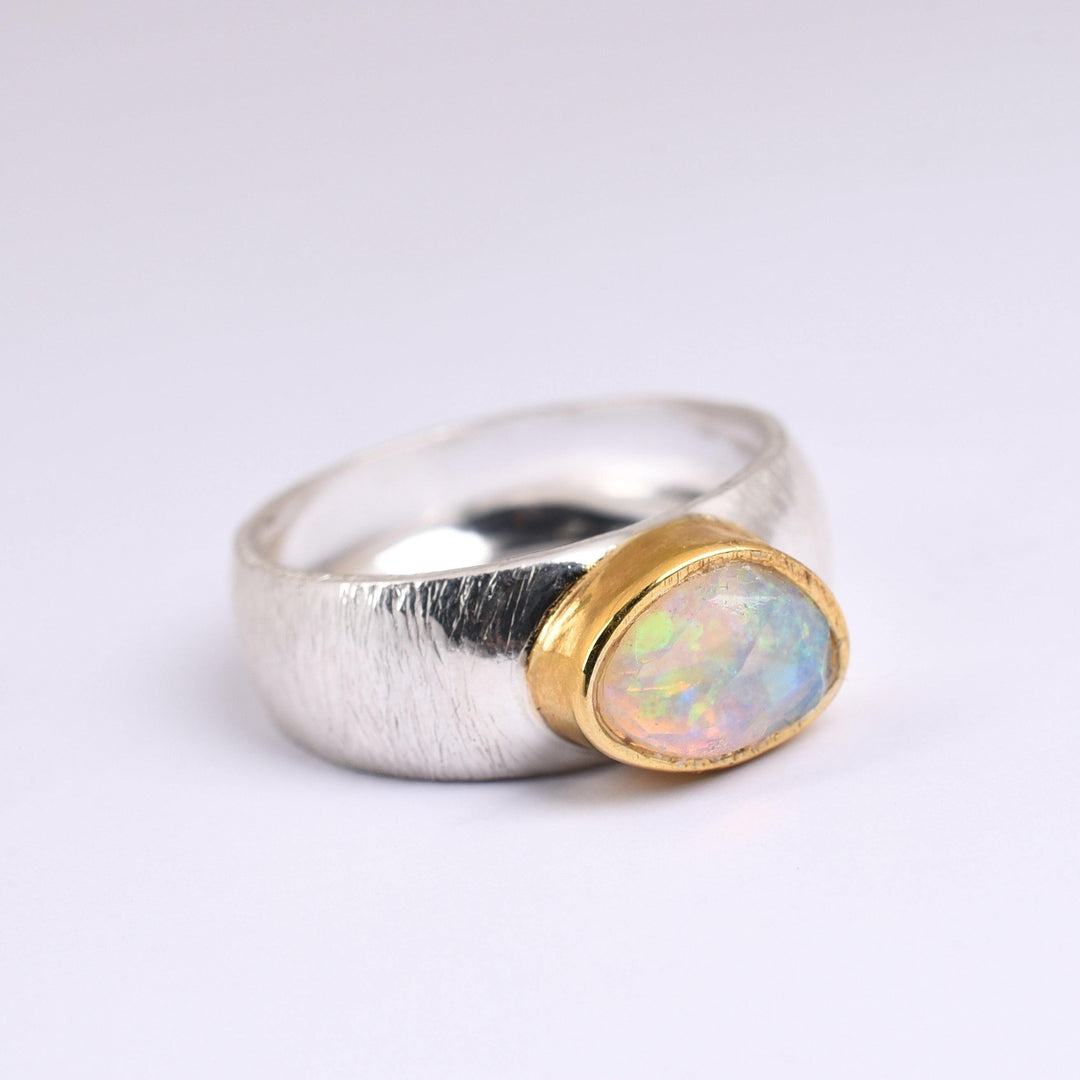 A Watermelon Tropical Ethiopian Opal Silver & Gold Ring with a wide, silver etched band featuring a central iridescent Ethiopian opal gemstone set in a gold vermeil bezel. The ring's design masterfully combines silver and gold elements, highlighting the colorful opal against a plain white background.