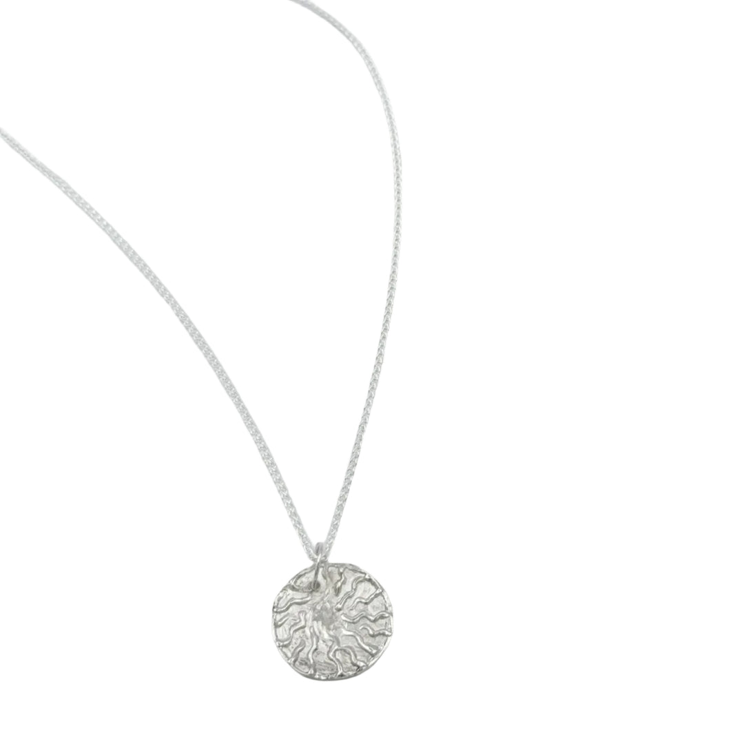 The Dara Pendant by Soufana Attia is a silver necklace with a round, textured pendant showcasing an abstract sun design symbolizing strength and heritage, shown on a white background.