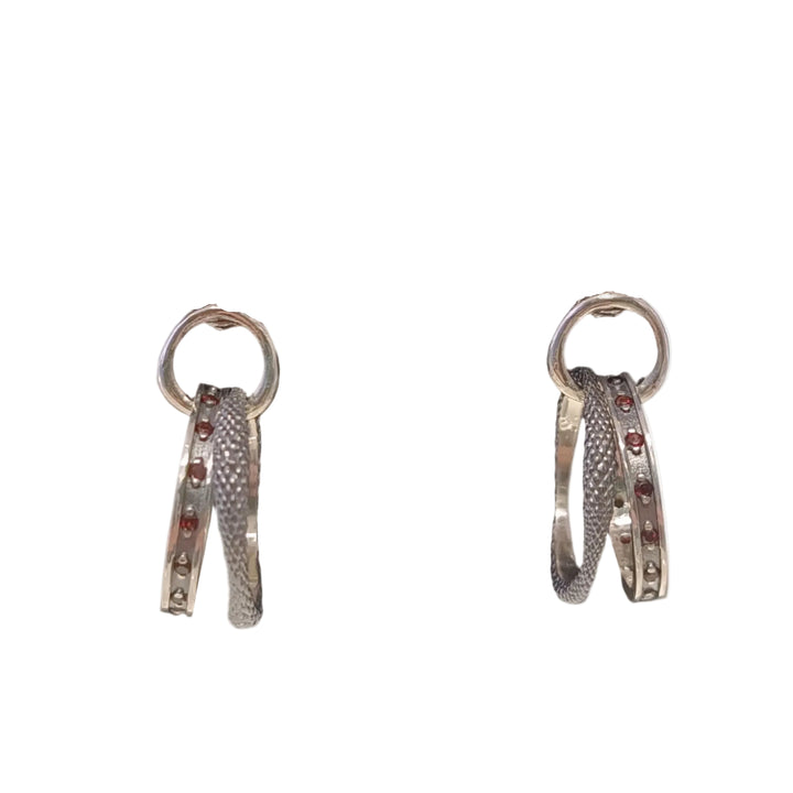 The K.And Double Circle Oxidised Earring with Red CZ features sterling silver textured bands adorned with red cubic zirconia and white stones along the edges, showcased on a white background.