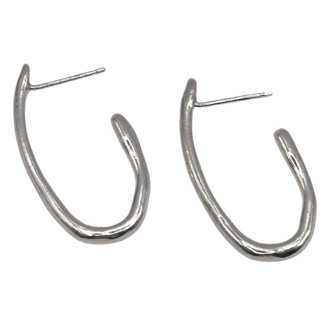 The Drop Organic Hoop Earrings by Inó Jewellery are handmade matte silver earrings with posts for pierced ears, featuring an irregular shape and rustic, hand-formed look—perfect for your unique collection.
