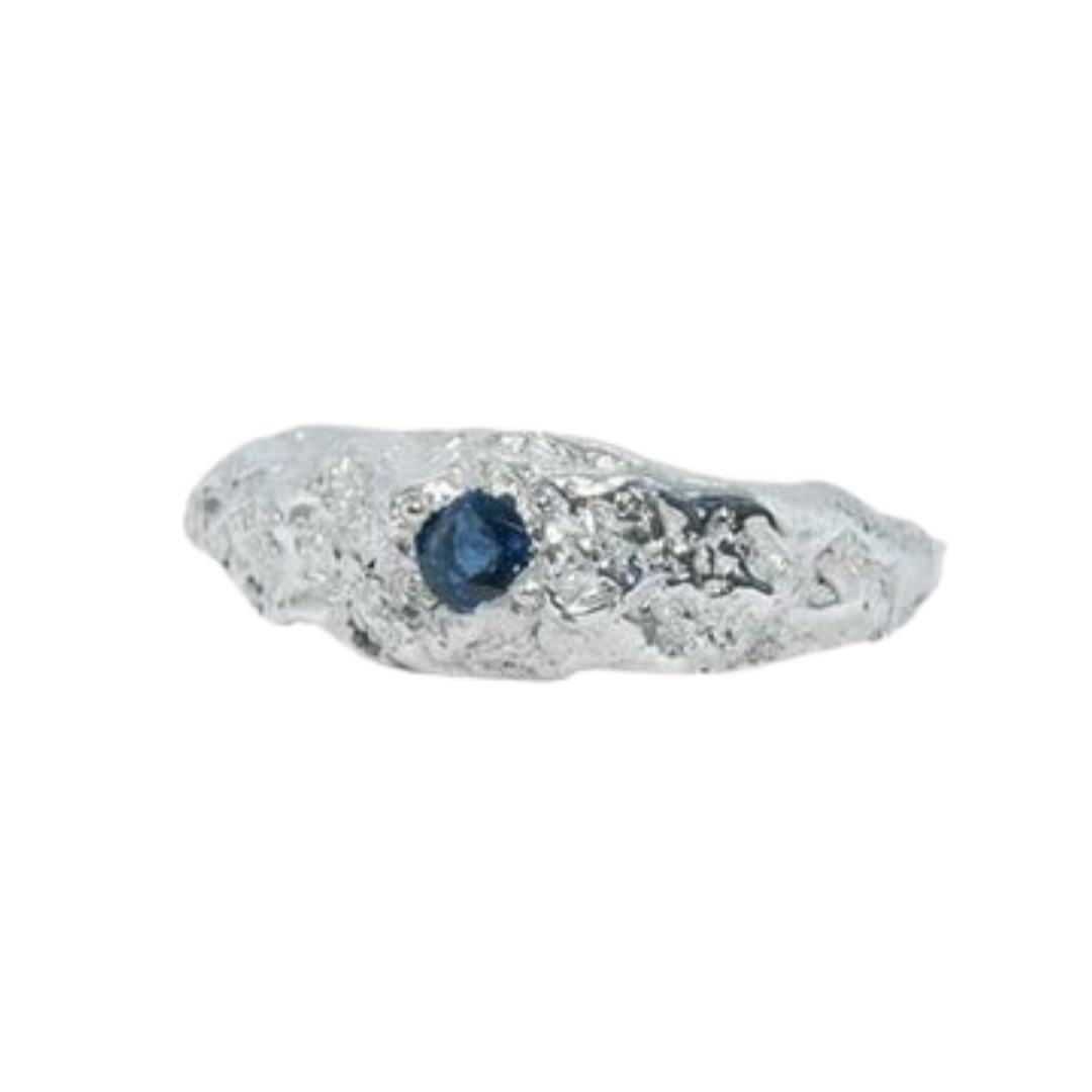 The Dublin Bay Silver Ring with Sapphire by Ava Jane Jewellery is a handmade sterling silver ring with an organic, textured shape and a small round sapphire set into the band, shown on a white background.