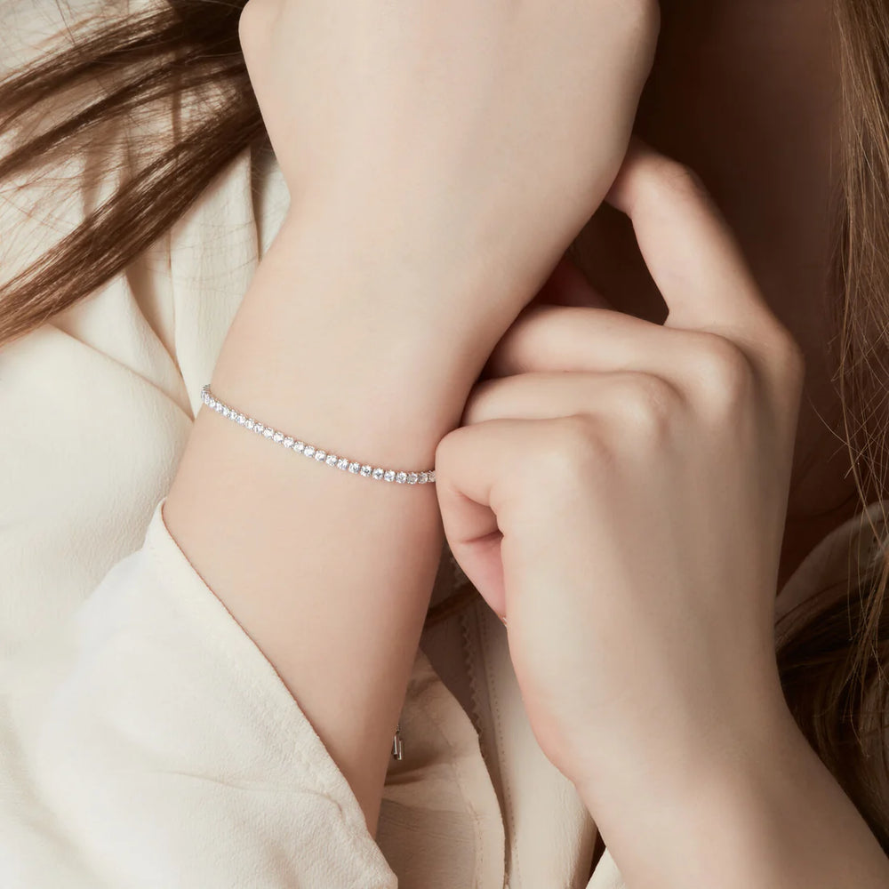 A close-up of a wrist wearing the Sif Jacobs Ellera Tennis Bracelet Silver, featuring small round gemstones and an adjustable slider clasp, styled against a cream long-sleeve top with hair partially visible.