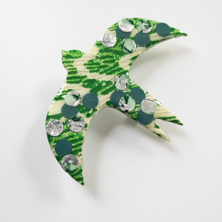 A handmade **Éan Bird Batik Textile Brooch** with green and white coloring, decorated with silver circular sequins and green dots, boasts an eco resin finish and unique texture, set against a plain white background by **Rothlú**.