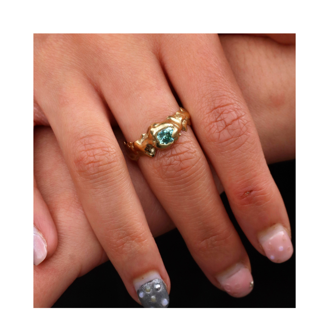 A hand with pastel-coloured, decorated nails wears the Madeleine Blaine Element Ring with Moissanite Small—an elegant, handmade one-off piece. A