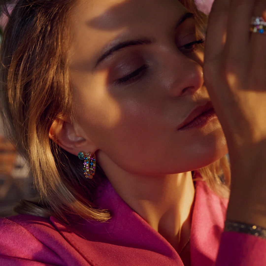 A close-up of a woman with blonde hair wearing a bright pink blazer and Sif Jacobs Ellisse Carezza Stud Earrings. Warm sunlight casts soft shadows on her serene face as she holds her hand near her lips.