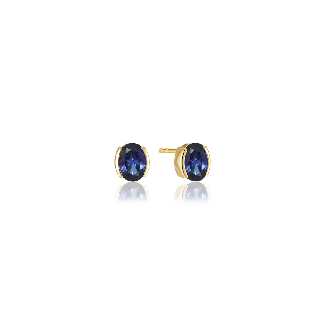 The Ellisse Carezza Stud Earrings by Sif Jacobs feature oval-shaped deep blue gemstones set in 18k gold plating, shown against a white background with a subtle reflection.
