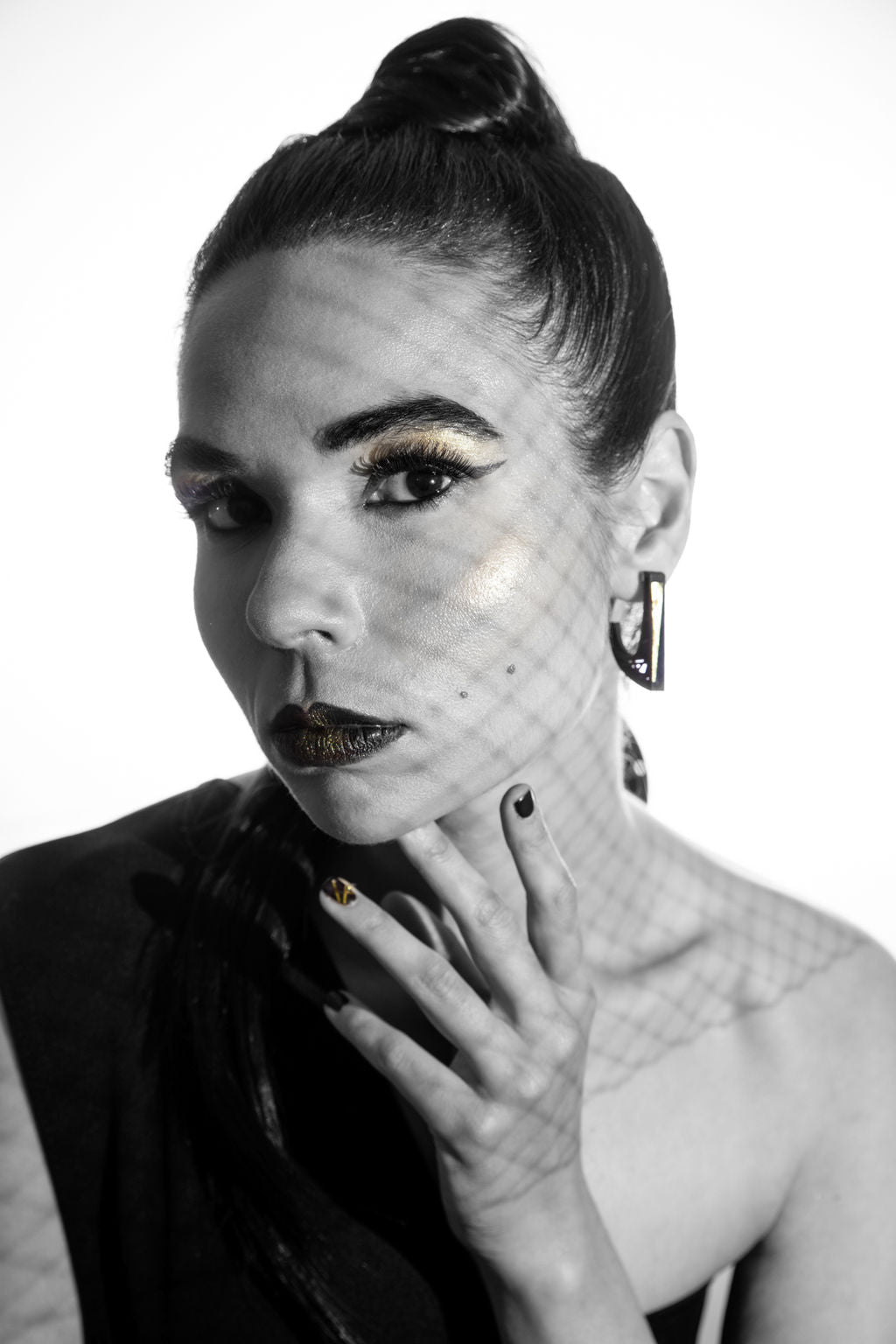 Black and white portrait of a woman with stylish makeup and a high ponytail. She has bold eye makeup, dark lipstick, and is wearing an off-shoulder top with Elsiem's Hebo Earrings featuring sterling silver ear posts. Her hand, decorated with nail art, is near her face, casting a patterned shadow.