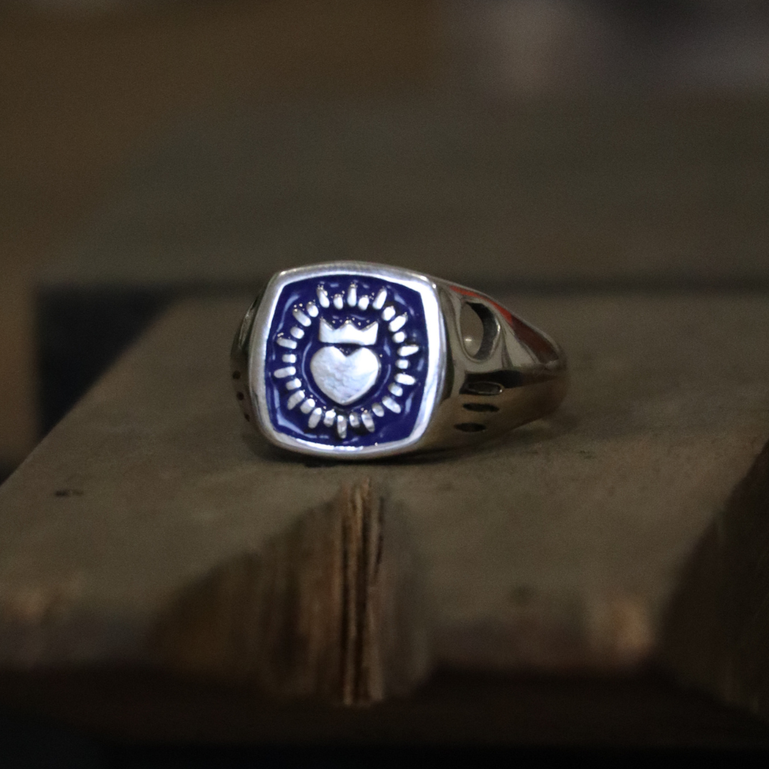 The Collective Dublin's Enamel Keith Haring Inspired Claddagh Ring features a dark blue square face with a central heart and sunburst design, taking cues from traditional handmade Dublin jewelry.