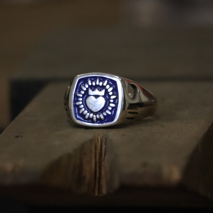 The Collective Dublin's Enamel Keith Haring Inspired Claddagh Ring features a dark blue square face with a central heart and sunburst design, taking cues from traditional handmade Dublin jewelry.