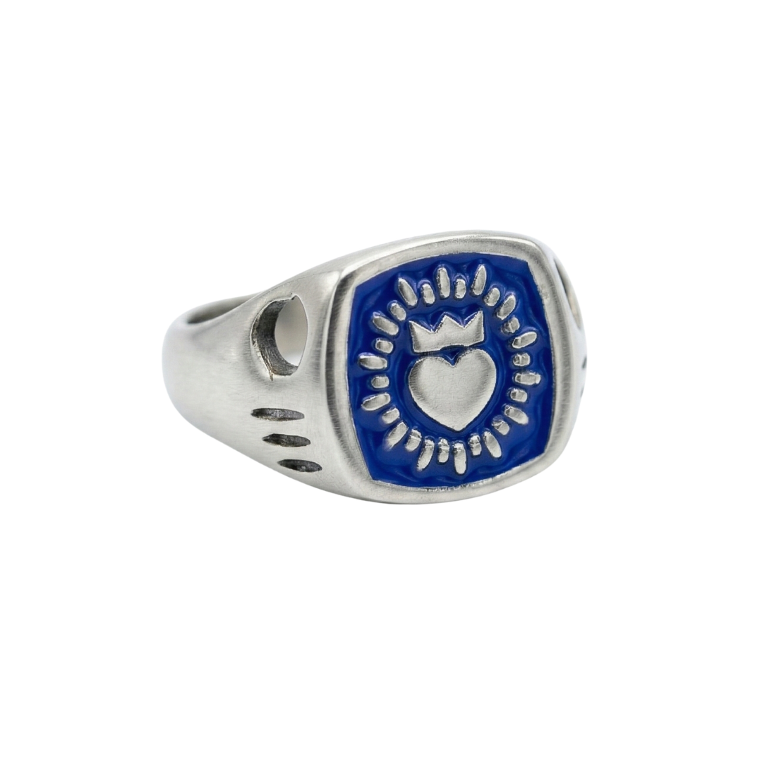 The Collective Dublin’s Enamel Keith Haring Inspired Claddagh Ring features a blue rectangular face with a raised crowned heart, circular motif, and three black dots per side—a handmade blend of tradition and modern flair.