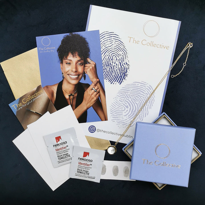 Promotional materials from "The Collective" show a woman wearing personalized jewelry, including an Engraved Fingerprint Pendant by Personalised Charms, and business cards. A light blue box, brochures with fingerprint designs, a necklace box, and towelettes complete the display.