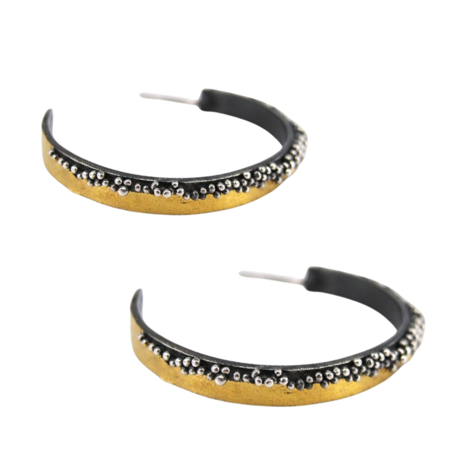 Two semi-circular hoop earrings featuring a gold-tone band adorned with small silver beads along the edge. The Etrusc Hoop Earrings by MarCucurella, showcasing an Etruscan granulation technique, have a black inner lining and exhibit a modern, stylish design that embodies the essence of handmade jewelry.