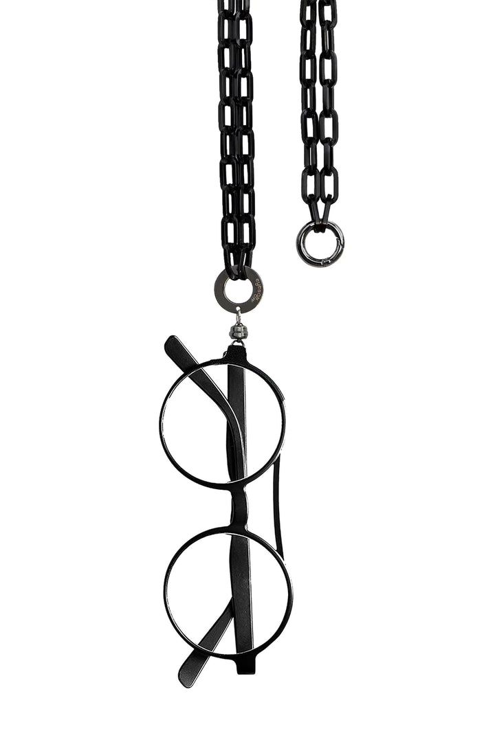 A pair of black round eyeglasses hangs elegantly from a smart necklace with wide, oval links and a clasp at the top. The EyesOnOff Eyewear Black Paperclip Chain by AnnaeAlex, suspended by one arm, showcases Italian craftsmanship against a pristine white background.