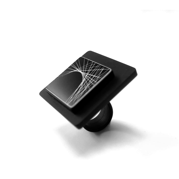 Introducing the Alex + Svet Frey Ring: a modern, square-shaped black accessory crafted from high-end acrylic. The flat, elevated top showcases an intricate geometric design with hand-drawn lines forming a symmetric pattern. The striking contrast of the ring against its plain white background highlights its elegance.