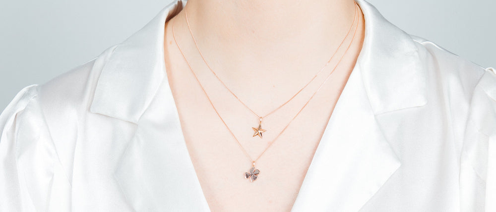 A person wearing a white satin blouse and two delicate gold necklaces—one with a star pendant and the other featuring Cosmic Boulevard’s Lucky Four Leaf Clover Silver Pendant, handmade in a Dublin studio.