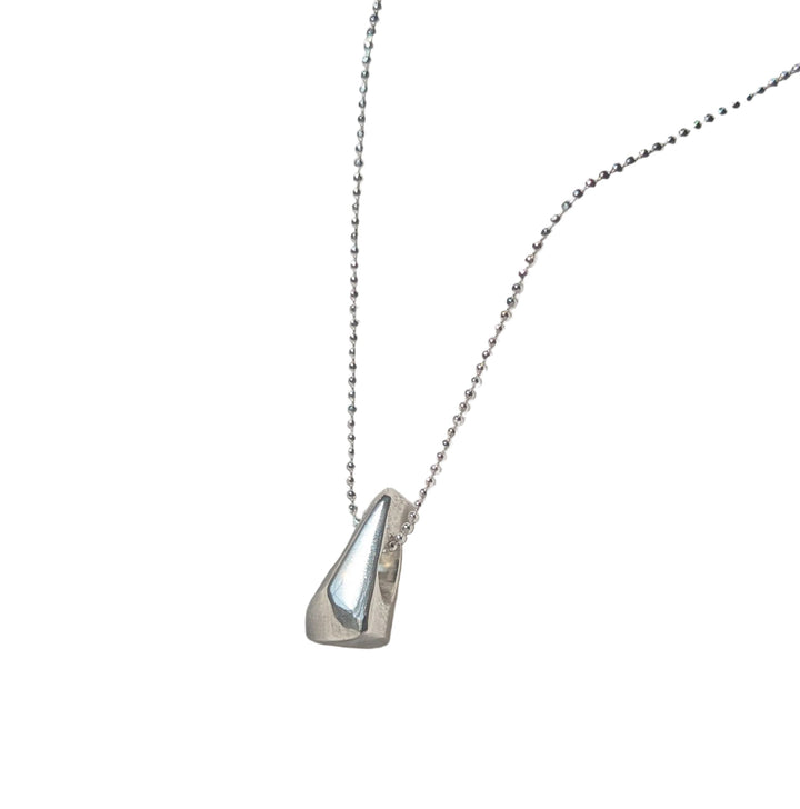 The Forbidden Facets Pendant by Becca Calmont, a handmade sterling silver teardrop on an 18-inch chain, is displayed on textured white fabric and softly lit by natural light.