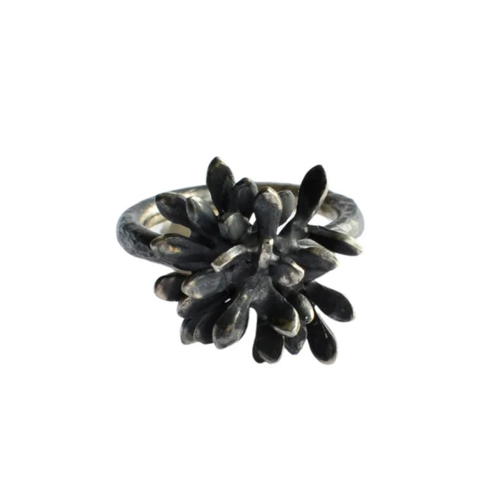 The Folia Oxidised Silver Ring by Abbie Dixon features an intricate, sculptural form with numerous small, petal-like elements radiating from the center, creating a textured, blossoming flower effect. The ring's darkened, oxidized Sterling silver finish adds an antique, artistic touch.