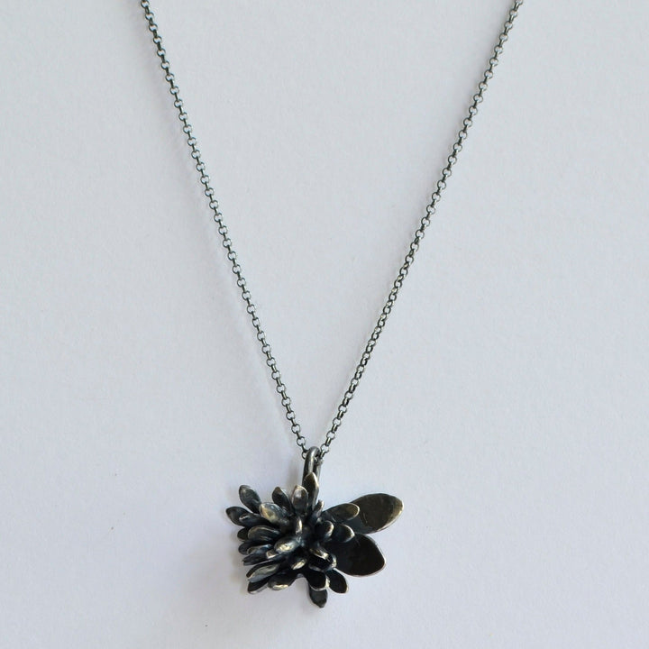 An Abbie Dixon Folia Oxidised Silver Pendant featuring a pendant shaped like a small, intricately designed flower with layered petals. The oxidised finish adds depth to the sculptural form, making it a stunning focal point against the plain white background.