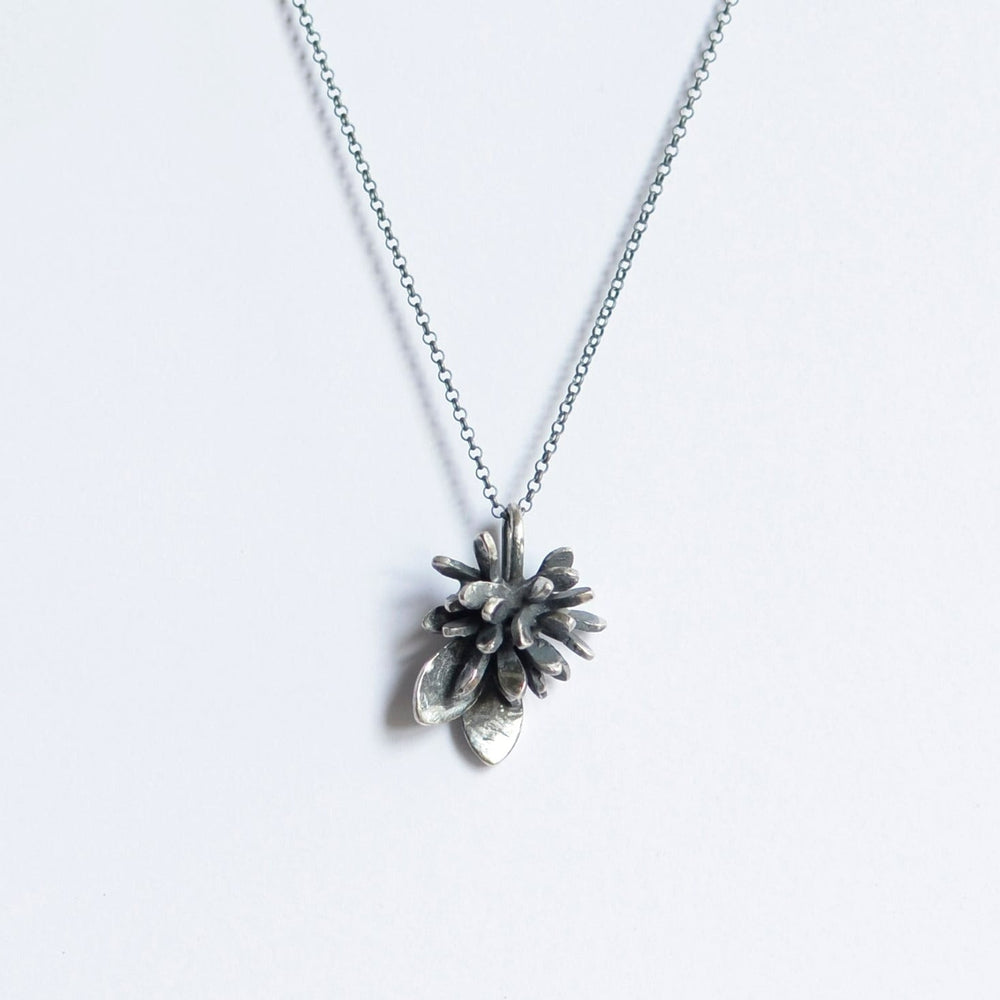 A delicate sterling silver necklace with a pendant shaped like a pine cone and two small leaves. The chain is simple and thin, and the sculptural form of the Abbie Dixon Folia Oxidised Silver Pendant hangs centrally on a plain white background.