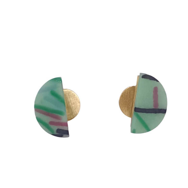 A pair of Funfetti Gold Vertical Earrings in various colours, crafted by Beira by Irene Reyes, placed on a light pink BEIRA card. The recycled bottle glass earrings feature a semi-circle design with green, black, and 18-carat gold plated accents. The background surface is white, with part of a black object visible at the top and a pair of black shoes at the bottom.