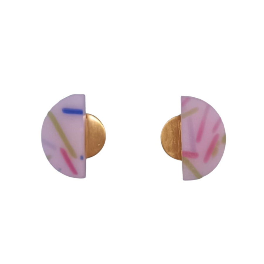 A vibrant pair of Funfetti Gold Vertical Earrings in pink, white, and blue abstract patterns feature a gold-colored half-circle design. Expertly crafted from recycled bottle glass and 18 carat gold plated, they are showcased on a light blue card adorned with "BEIRA" and "by Irene Reyes." The background provides a partial glimpse of shoes and the floor.