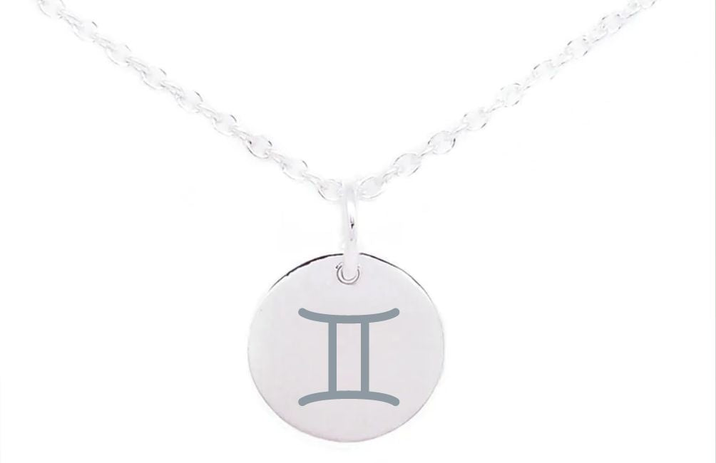 A silver necklace with a round pendant featuring the Gemini zodiac sign in the center. The pendant, showcasing sterling silver charms, is attached to a delicate, twisted chain. The background is white. This stunning piece is the "Horoscope Large Disc Charm Silver" by Personalised Charms.