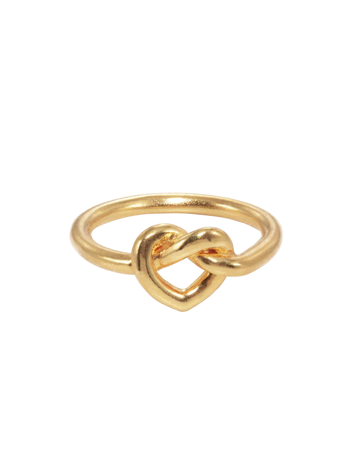 The Jane Koenig Tied Heart Ring is a gold ring with a heart-shaped knot design at the center, shown on a plain white background.