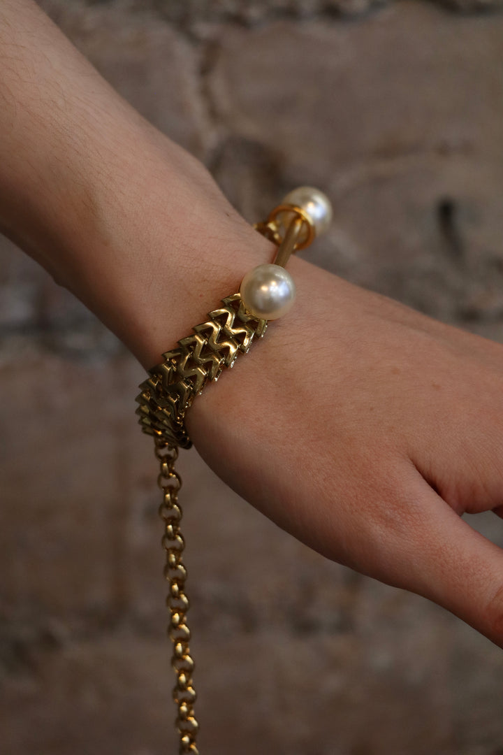 A close-up of a hand wearing the Zubeldia Gold Bar and Double Pearl Chunky Bracelet, featuring a chunky gold chain with two large pearls at each end, set against a blurred stone background.