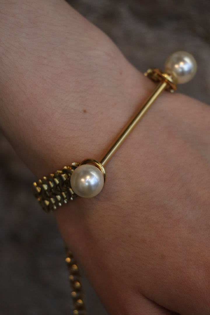 A close-up of a wrist wearing the Zubeldia Gold Bar and Double Pearl Chunky Bracelet, featuring a textured gold band with two large pearl-like beads; the elegant design stands out against a blurred background.