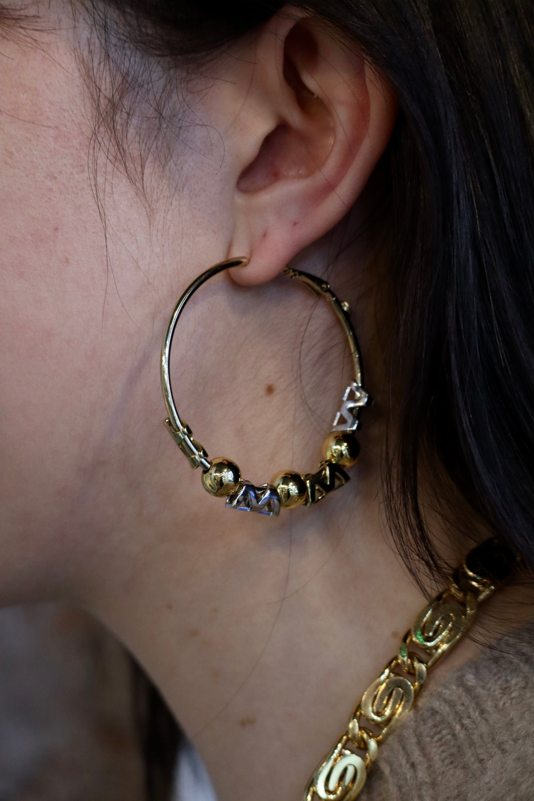 A close-up of a person with long dark hair wearing Zubeldia Gold and Silver Hoop Earrings and a chunky gold necklace.