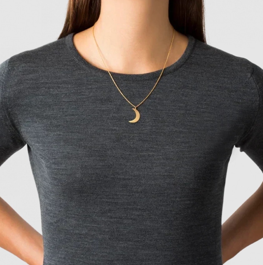 A gold crescent moon pendant necklace worn by a model in a dark gray crewneck t-shirt against a light gray background.