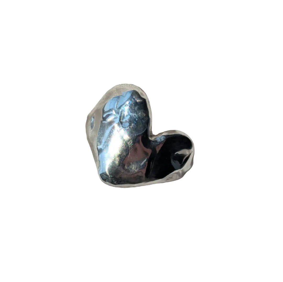 The Gra Heart Ring by Becca Calmont features a shiny, handcrafted design made from recycled silver, shown gleaming with soft shadows on textured white fabric.