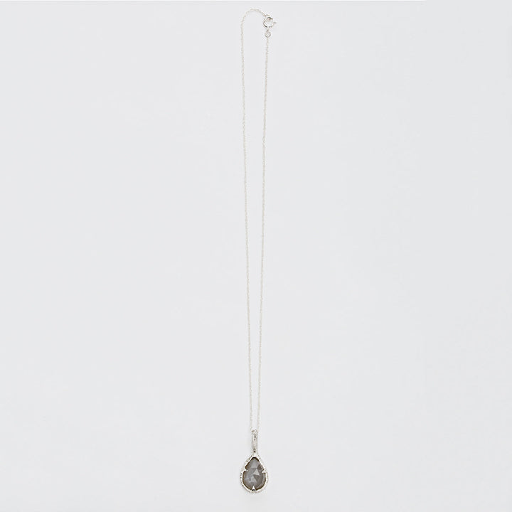 A delicate sterling silver chain necklace with a teardrop-shaped, faceted dark gemstone pendant. The Thorn Teardrop Pendant by Abbie Dixon, which evokes the elegance of a moonstone's glimmer, is displayed against a plain white background.