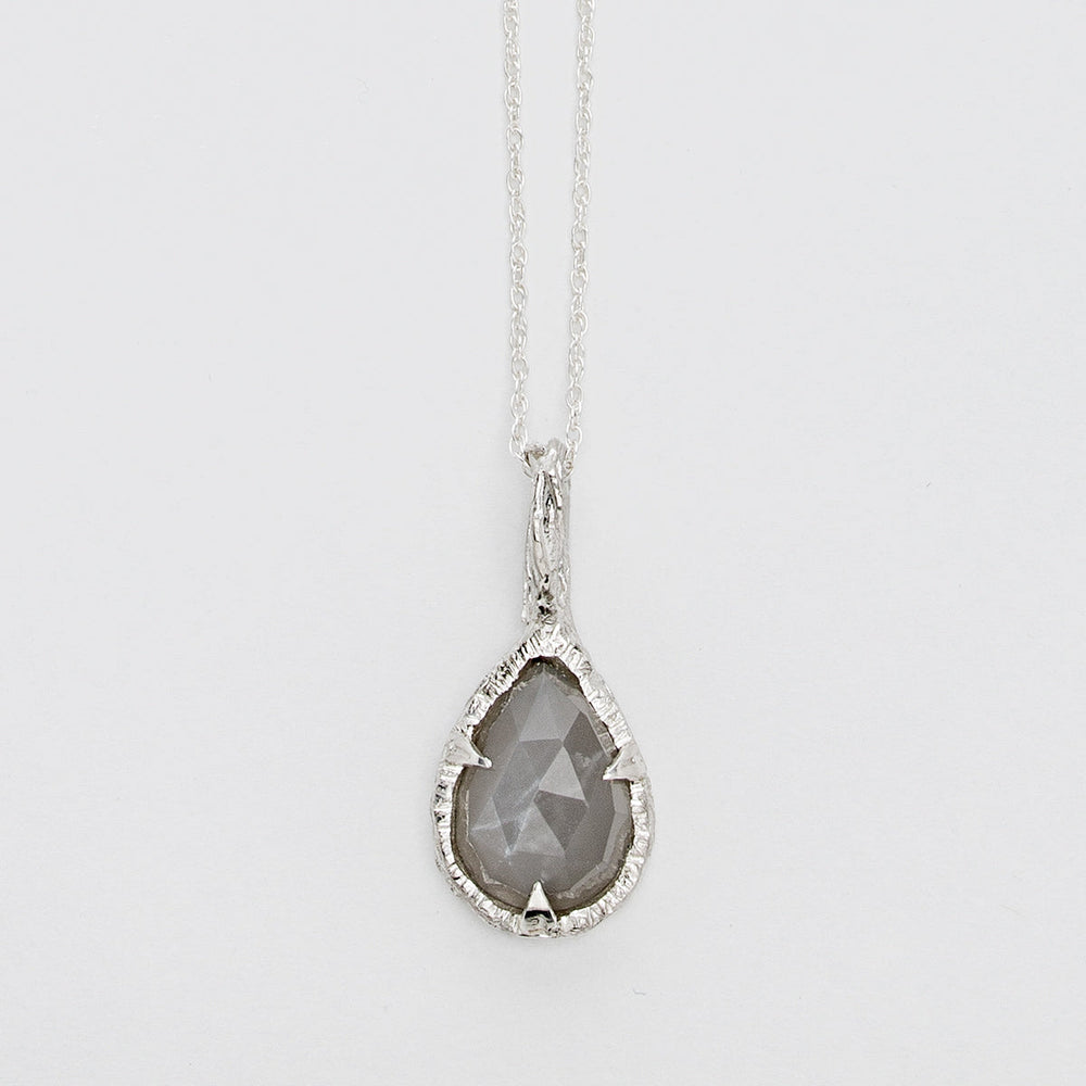 A delicate sterling silver necklace features **the Thorn Teardrop Pendant by Abbie Dixon**, with a faceted gray moonstone. The pendant is set in an intricately textured silver frame, hanging from a thin, elegant chain against a plain white background.