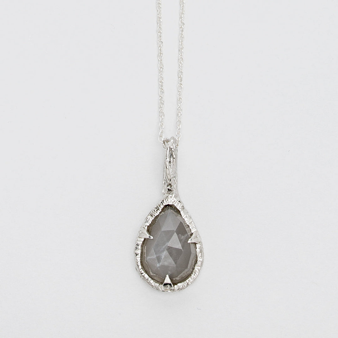 A delicate sterling silver necklace features **the Thorn Teardrop Pendant by Abbie Dixon**, with a faceted gray moonstone. The pendant is set in an intricately textured silver frame, hanging from a thin, elegant chain against a plain white background.