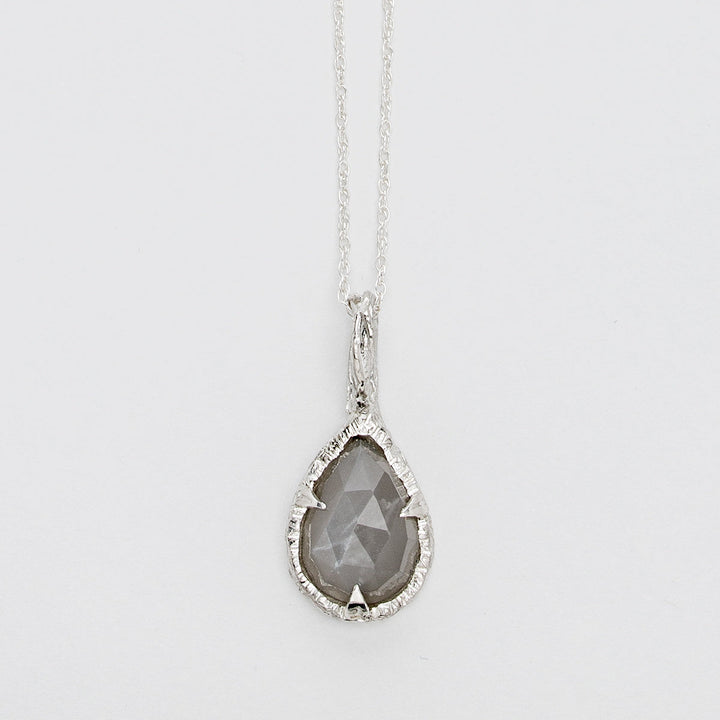 A delicate sterling silver necklace features **the Thorn Teardrop Pendant by Abbie Dixon**, with a faceted gray moonstone. The pendant is set in an intricately textured silver frame, hanging from a thin, elegant chain against a plain white background.