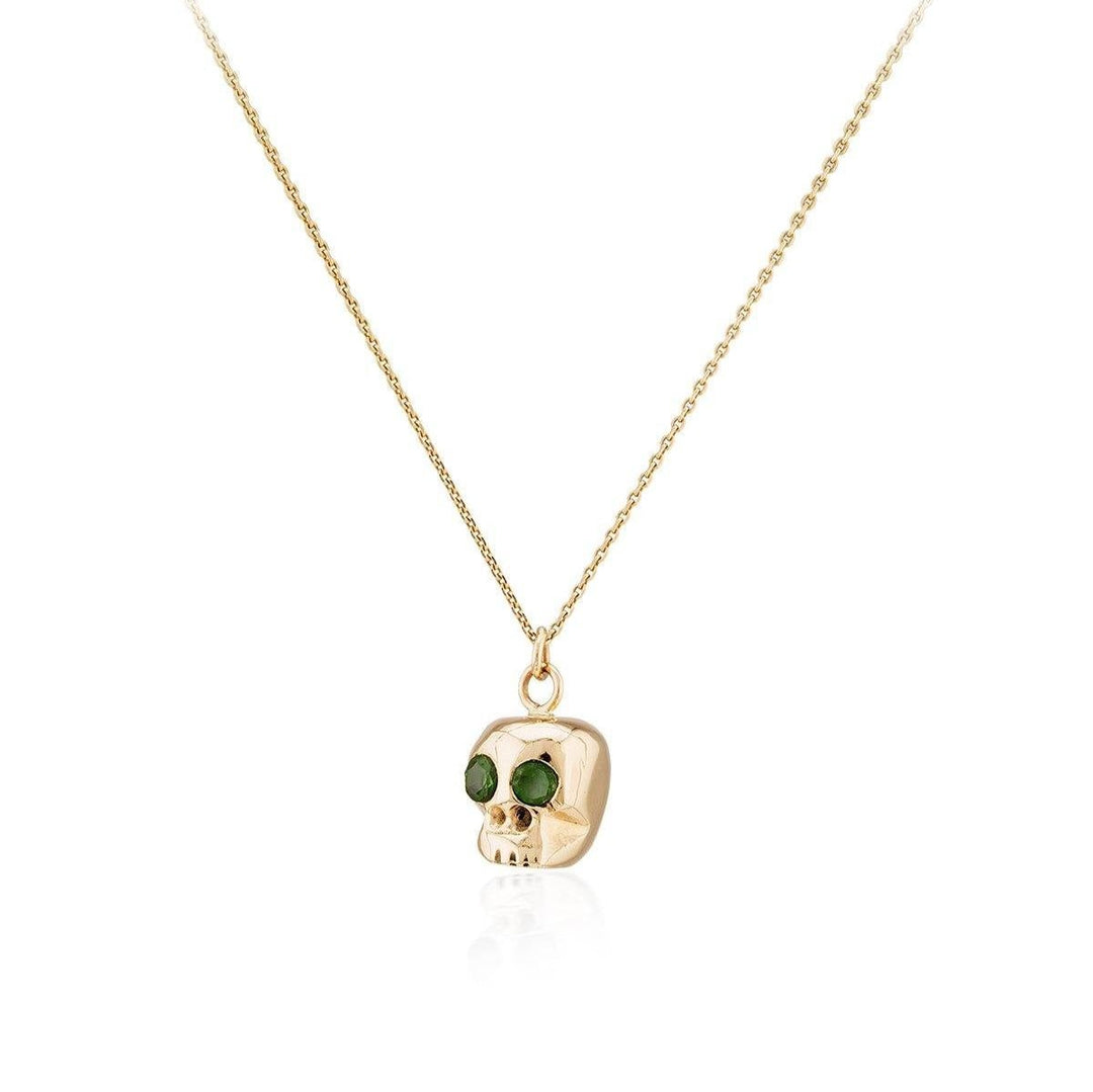 A 9ct gold necklace with a delicate chain featuring a Gold Memento Mori Skull Pendant, crafted by Dublin Studio under the prestigious brand Cosmic Boulevard. The skull boasts two green gemstones set as eyes, making it an exquisite piece of handmade jewellery. The white background ensures the necklace remains the focal point of the image.