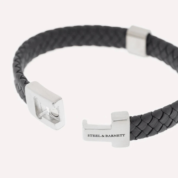 Perfect for the modern professional, the Harrison - Black bracelet by Steel and Barnett combines sophistication and style. It features a black braided Nappa leather band with sleek silver hardware. The clasp proudly displays the brand name "STEEL AND BARNETT" engraved on one end, showcasing its elegant weave and contemporary design.