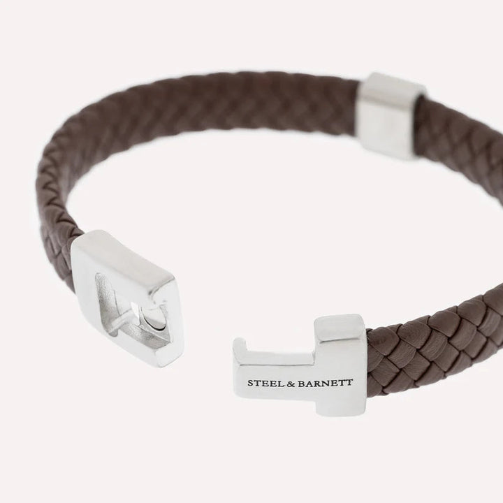 The Harrison - Brown bracelet by Steel and Barnett showcases a brown braided Nappa leather band with a silver, angular, modern clasp engraved with "Steel & Barnett," elegantly presented on a plain white background.