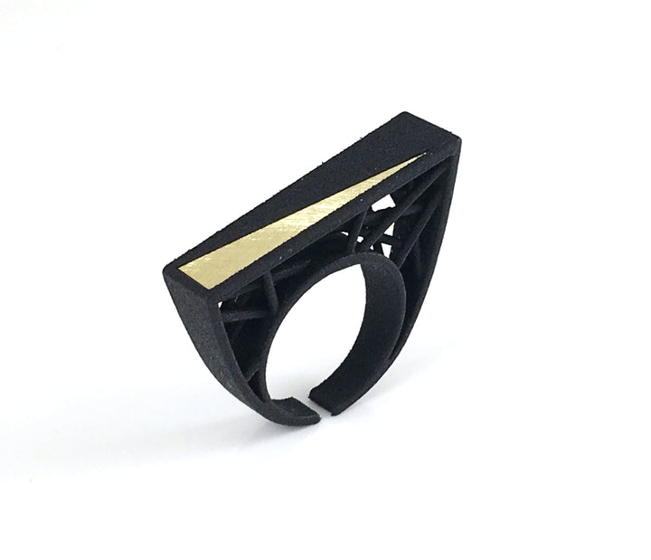 A modern, geometric black ring featuring an open circle band and a sleek, rectangular top with a gold diagonal stripe. 3D printed in SLS Nylon, the design showcases clean lines and an architectural, contemporary style reminiscent of Barbara Hepworth's artistry. Set against a plain white background. Introducing the Hebo Statement Ring by Elsiem.