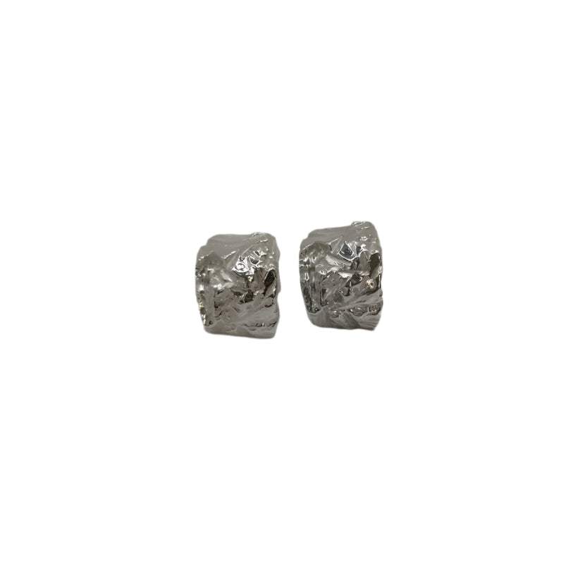 Two small, irregularly shaped Hephaestus Earrings by Inó Jewellery, crafted in crumpled sterling silver and evoking handmade statement pieces, are placed side by side on a plain white background.