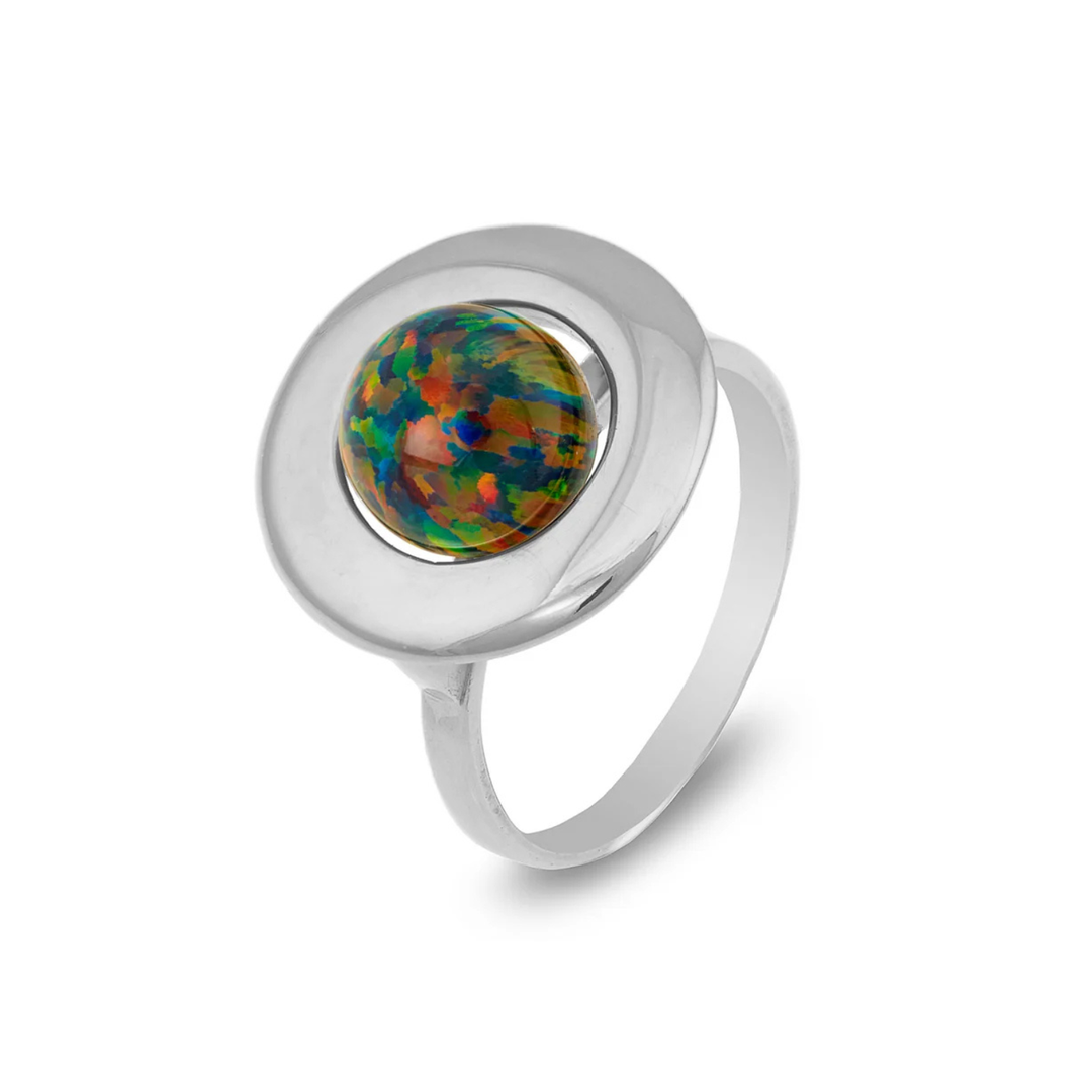 The Cosmic Boulevard Home Planet Black Opal Sterling Silver features a round, iridescent opal stone set in the center. The opal displays a vibrant mix of red, green, and blue hues and is mounted on a flat, circular silver base. The band is simple and sleek, complementing the intricate opal design perfectly.