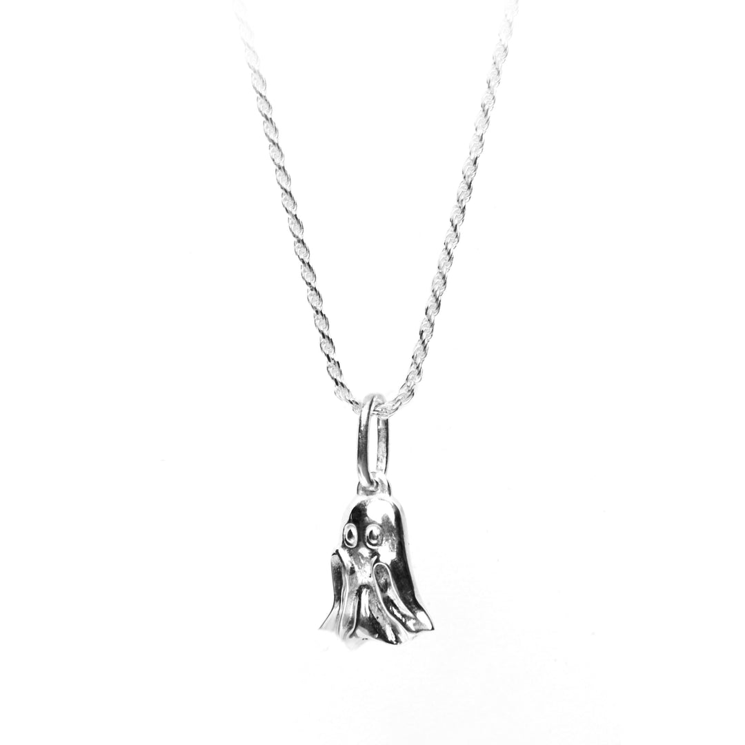 A delicate sterling silver necklace features a pendant shaped like a small, cute ghost with two eyes and slightly flared ends, adding a touch of spooky charm to the accessory. Hand-carved in a Dublin studio, the Lil Boo Silver Pendant by Cosmic Boulevard hangs from a twisted chain, highlighting its intricate design.