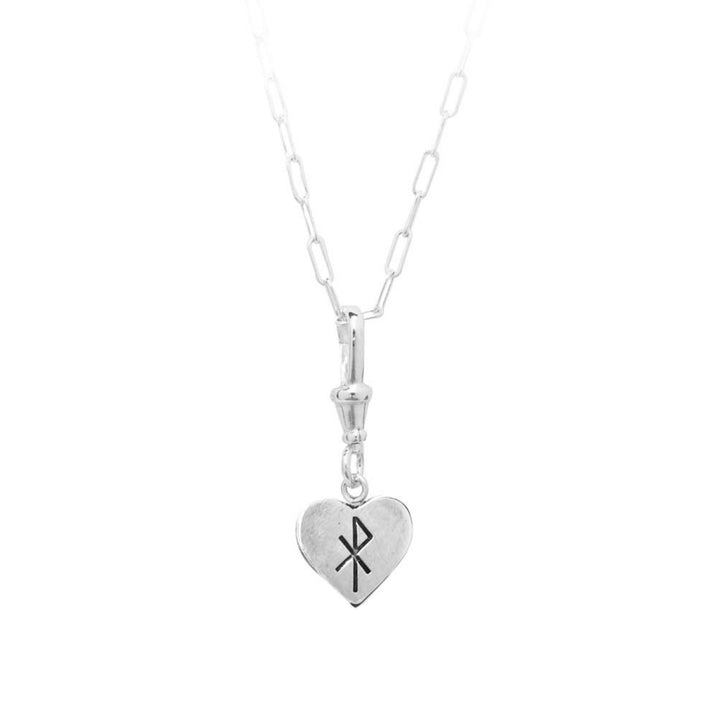 A silver necklace with an elongated link chain features a handmade and engraved heart-shaped pendant. The Lil Sad Grimm Silver Pendant by Cosmic Boulevard, which includes a Chi Rho symbol representing the Christian monogram formed by the first two Greek letters of “Christos,” complements any outfit beautifully.