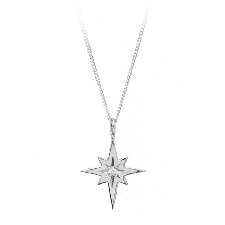 The Diamond Polaris Pendant by Cosmic Boulevard, crafted in sterling silver and shaped like an eight-pointed North Star, features a small, sparkling gem at its center. Attached to a thin, delicate chain, this piece of handmade jewelry boasts a minimalist and elegant design.