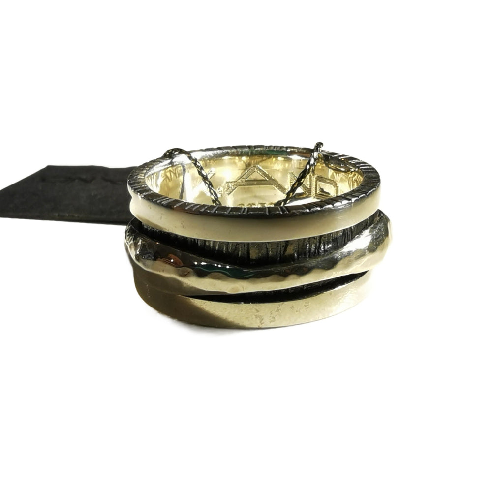 Three K.And Silver Spinner Rings with textured finishes are stacked on a white background. A black pouch is partially visible behind them, emphasizing the refined elegance of this K.And collection.