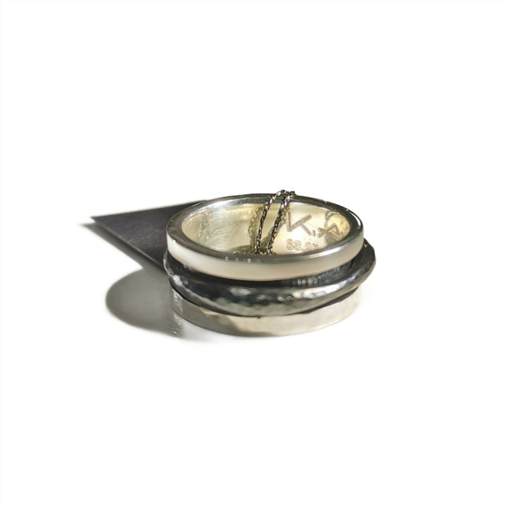 The Silver & Oxidised Single Spinner Ring by K.And features a hammered texture and thin chain accent, displayed on a white surface with a dark triangular shadow to the left.