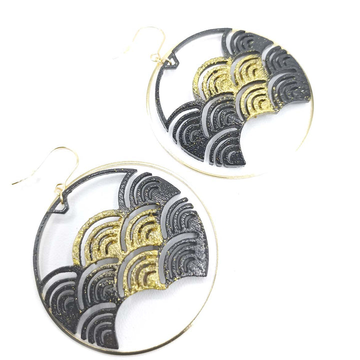 A pair of Black Japanese Wave Earrings by Tochu-De featuring an intricate geometric design with overlapping wave patterns in black and gold, 3D printed from nylon. The earrings are suspended from gold-colored hooks and displayed against a plain white background. To maintain their beauty, gently clean with a soft dry cloth.