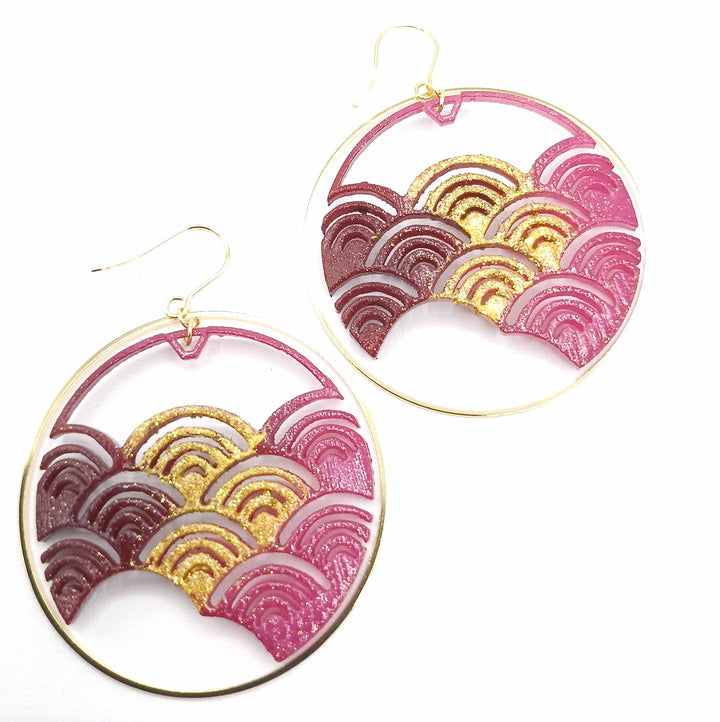 Fuchsia Japanese Wave Earrings with a transparent pink and gold wave pattern. The waves are arranged in gradient shades ranging from dark pink to gold within a thin gold circular frame. Each earring has a gold hook for wearing. This intricate, eye-catching design is a stunning piece of 3D printed nylon jewellery from Tochu-De.