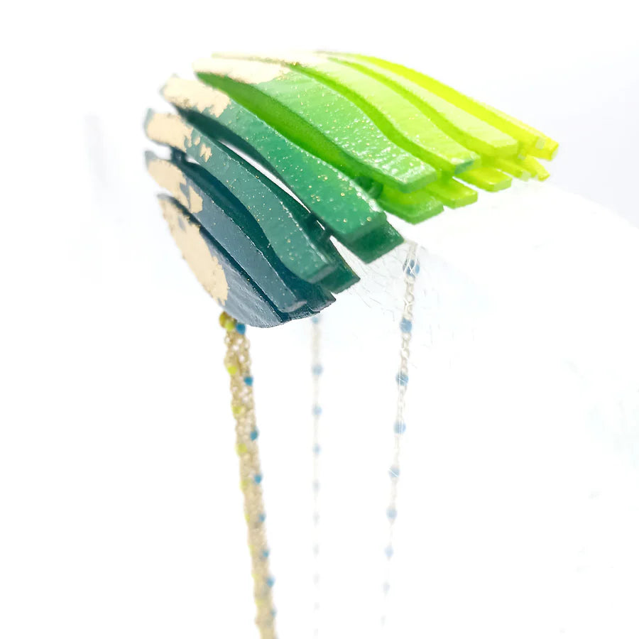 Close-up of Tochu-De's Long Circle Wave Necklace in Petrol & Citrus: layered green and yellow resin with gold accents, arched on white. Thin beaded strands hang below, creating a striking statement necklace.